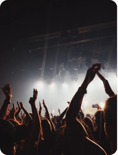 Publikum på en konsert som løfter hendene og danser under fargerik scenebelysning.